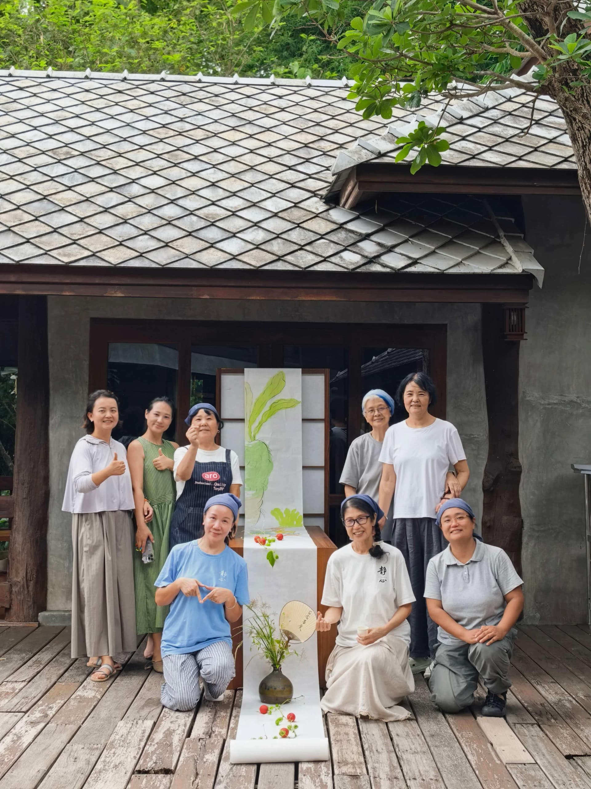 八人在传统泰式建筑前合照,身旁放置插花装置