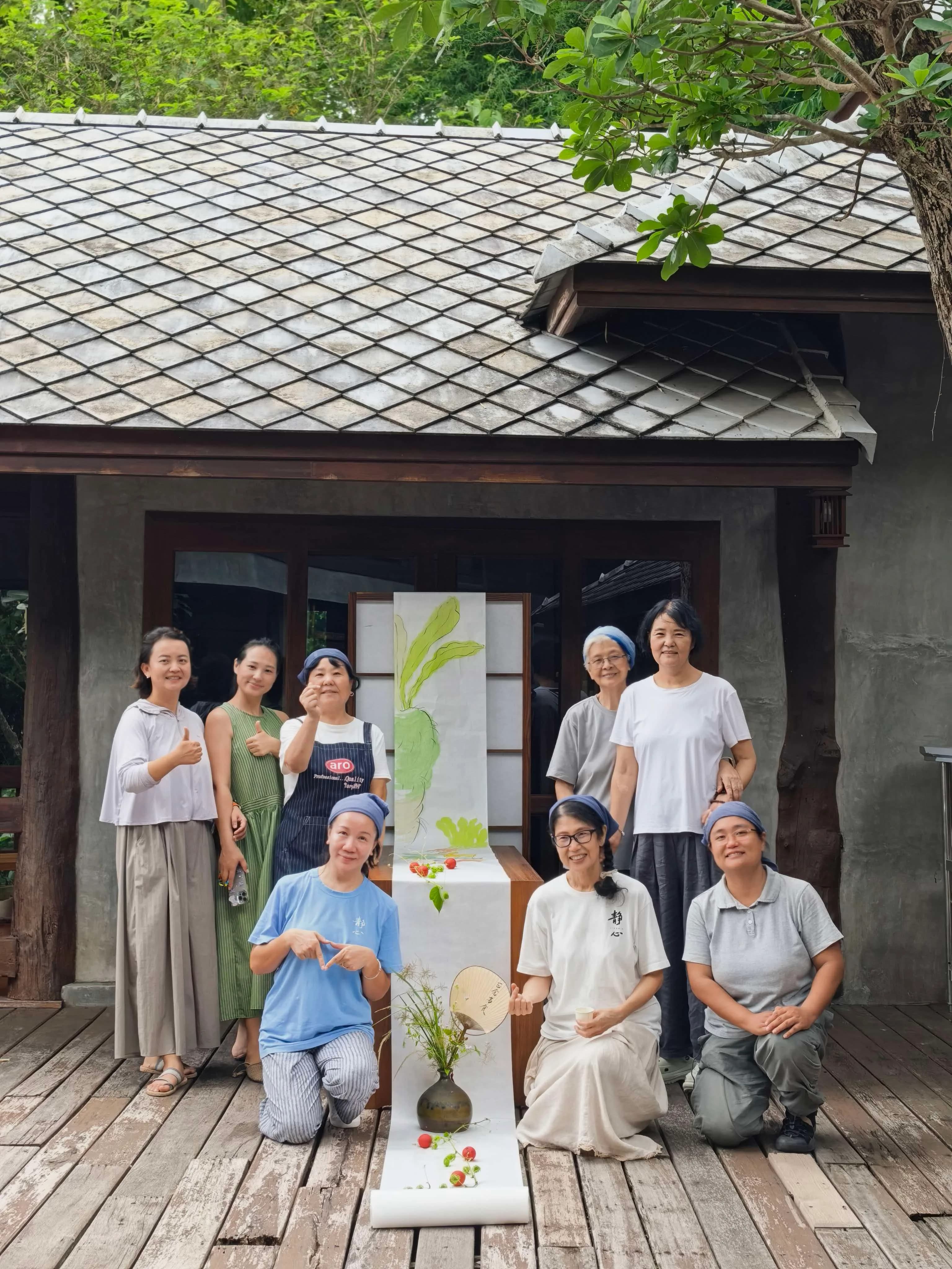八人在传统泰式建筑前合照,身旁放置插花装置