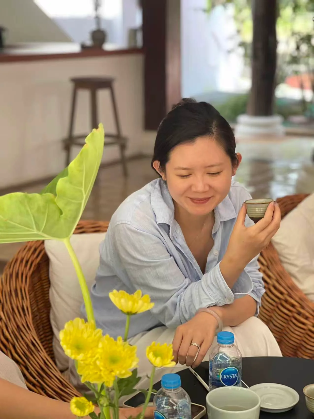 女性在室内坐着品茶,面前放着黄花和水杯