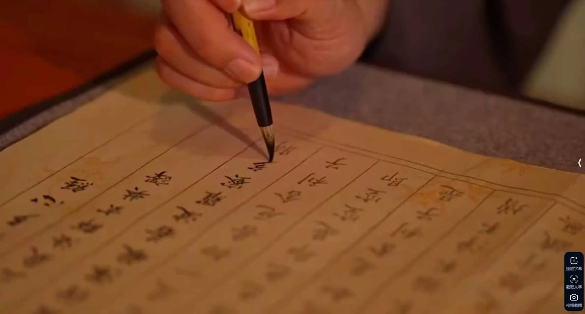 Hand holding a calligraphy brush writing Chinese characters on cream-colored rice paper