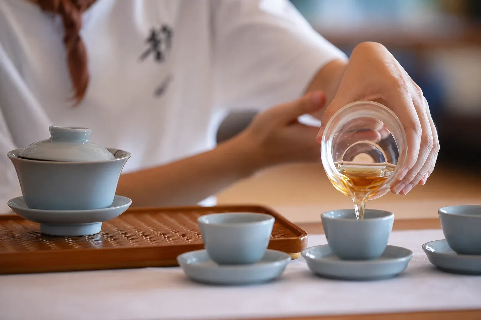 手持粉色茶壶向白瓷茶杯倒茶,茶具摆放在木制茶盘上