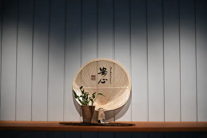 木制圆形扇子与陶土花盆和茶具摆放在木架上,背景为竖条纹墙面