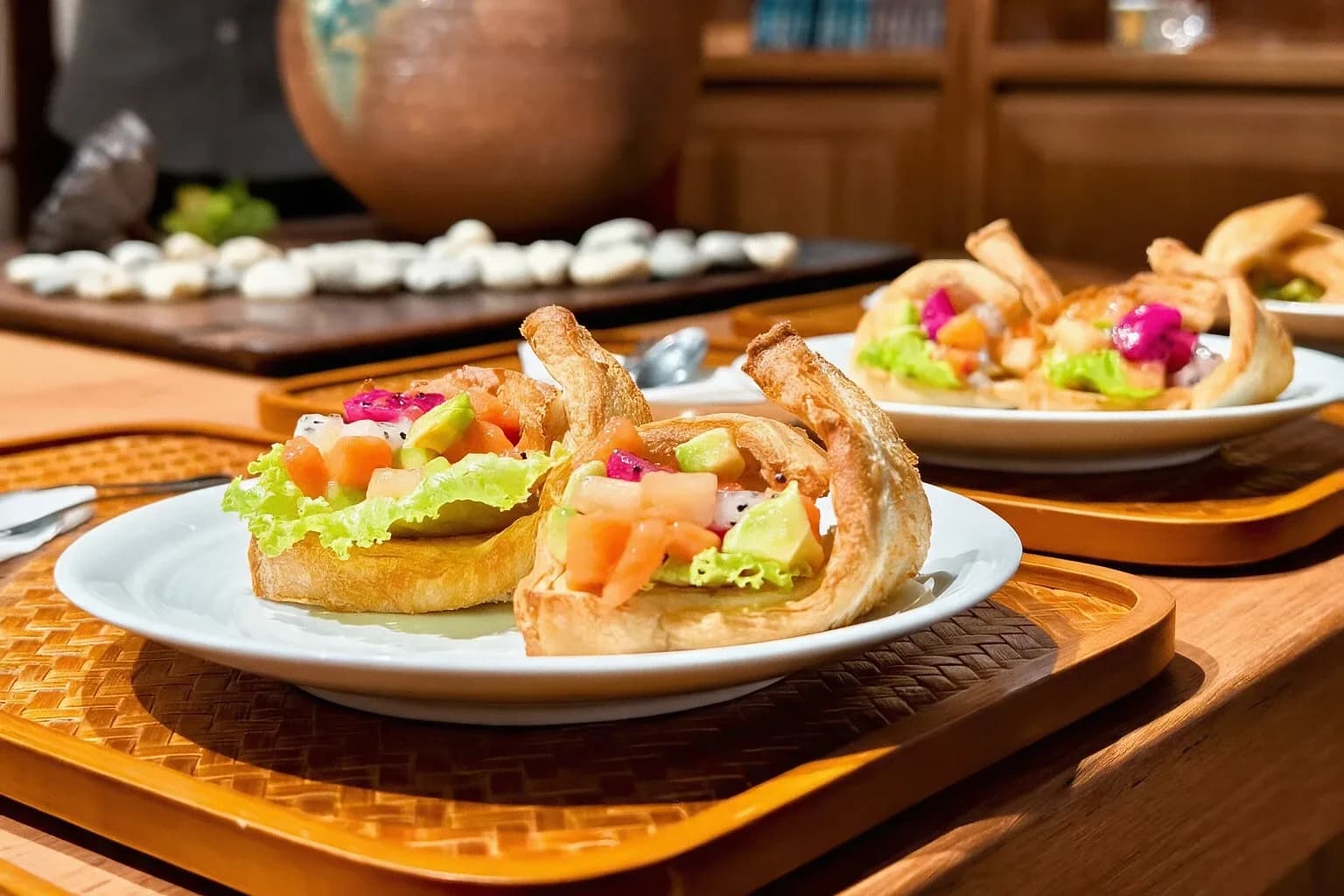 Fried shrimp paste cups filled with lettuce, diced vegetables, and colorful garnish served on white plates at a wooden dining table